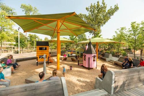 A vibrant playground with colorful play structures, shaded areas, and families enjoying the outdoor space.