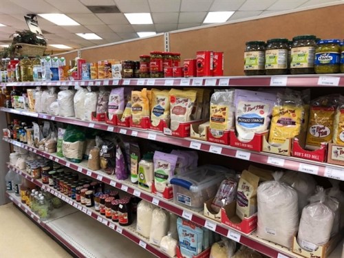 A grocery store aisle filled with various packaged food items, including grains, oils, and condiments on shelves.