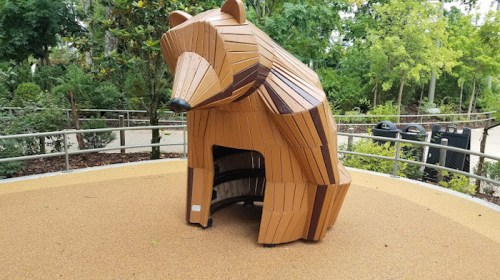 A wooden bear sculpture in a park, designed as a play structure with an open space underneath.