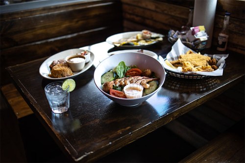 A wooden table with a variety of dishes: a salad, a bowl of soup, fried food, and a glass of water with lime.