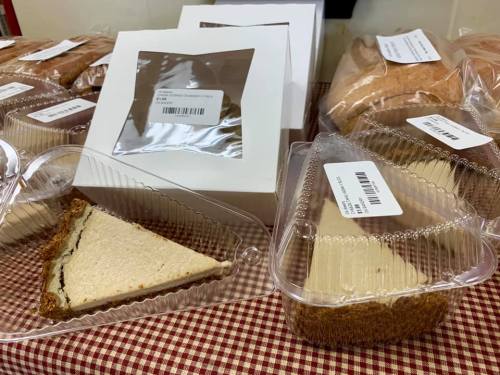 A table with packaged cakes and slices, some in clear containers, with labels on each item.