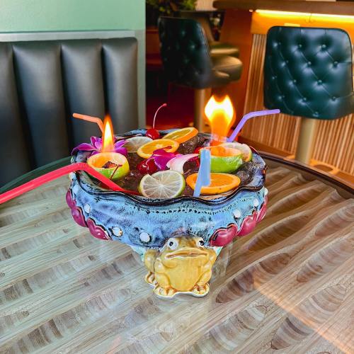 A colorful cocktail bowl with fruit garnishes and flaming drinks, resting on a wooden table.