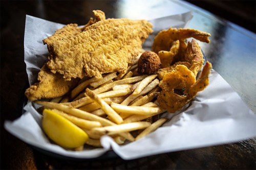 A plate of fried fish, shrimp, hushpuppies, and French fries, garnished with a lemon wedge.