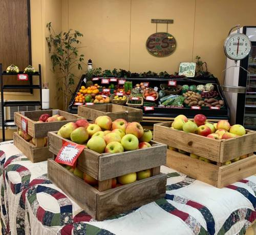 A display of wooden crates filled with apples, set in a market with various fruits and vegetables in the background.