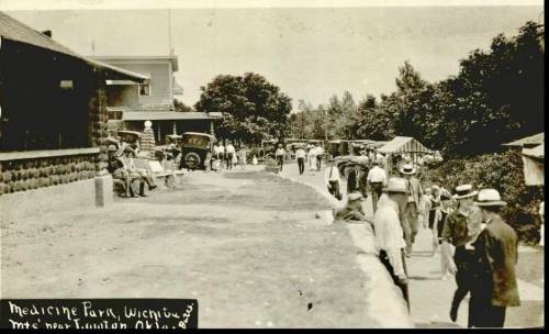 Historic black-and-white photo of a busy street scene in Medicine Park, Oklahoma, with people and vintage cars.