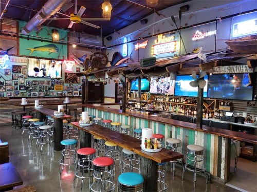 A vibrant bar interior with colorful stools, neon signs, and a rustic wooden counter, featuring a lively beach theme.