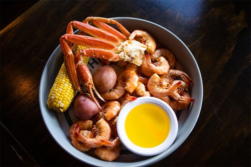 A seafood platter featuring shrimp, crab, corn, and potatoes, served with a small bowl of melted butter.