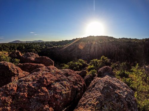 A sunlit landscape with rocky terrain and lush greenery under a clear blue sky.
