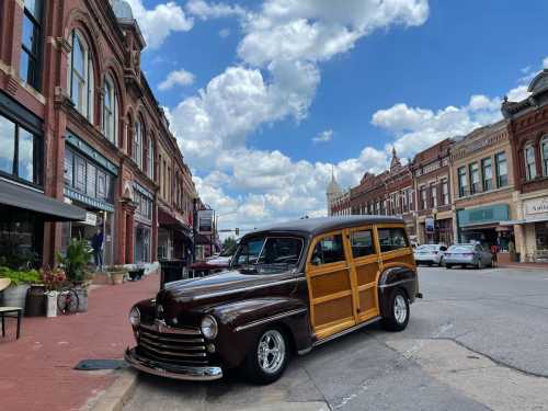 A vintage wood-paneled car parked on a charming street with historic buildings and a blue sky in the background.