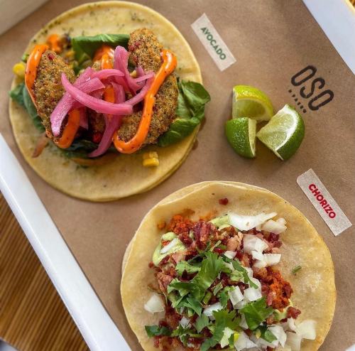 Two tacos on a tray: one with chorizo, onions, and cilantro; the other with avocado, greens, and crispy toppings.