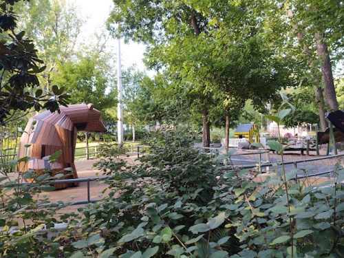 A playground featuring a wooden animal structure, surrounded by greenery and play areas for children.