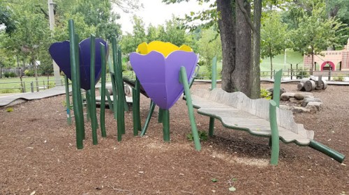 Colorful flower-shaped play structures surrounded by greenery in a playground setting.