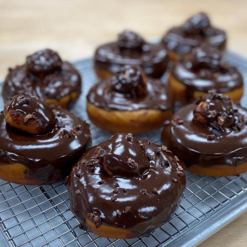 A tray of chocolate-glazed donuts topped with chocolate pieces and a small donut on each.