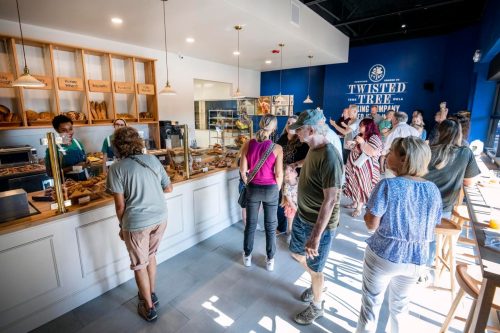 A busy bakery with customers lining up at the counter, browsing a variety of baked goods. Bright and inviting atmosphere.