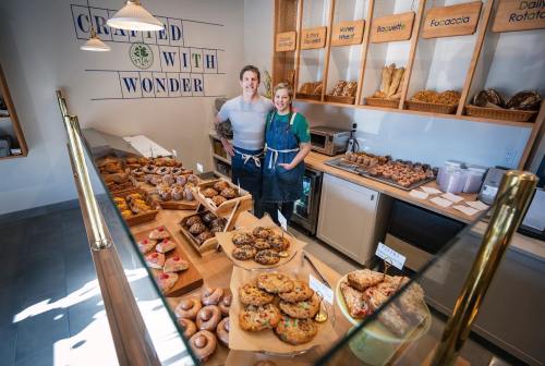 A bakery display filled with various baked goods, featuring two smiling staff members in front of the counter.