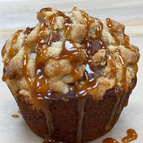 A close-up of a muffin topped with crumbled streusel and drizzled with caramel sauce.