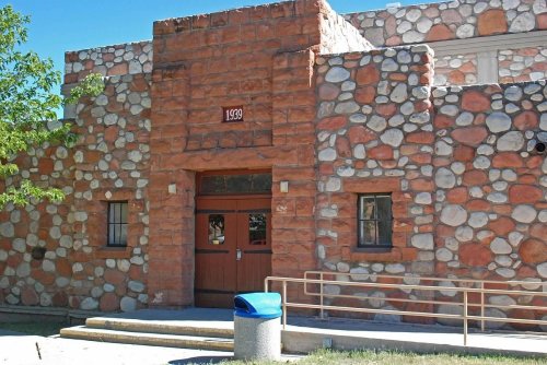 A stone building with a wooden door, marked "1939," and a blue trash can in front.