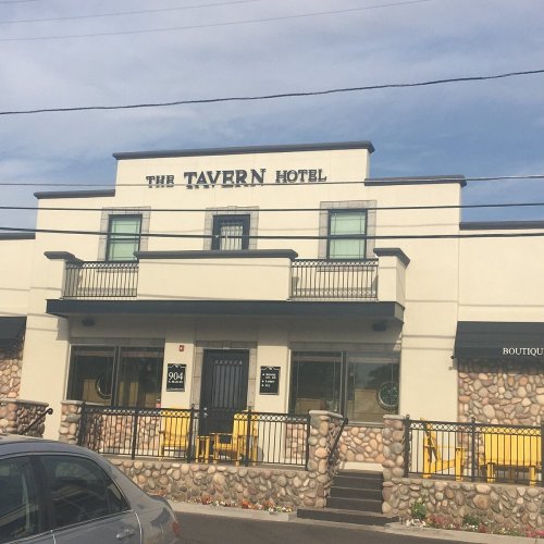Exterior of The Tavern Hotel, featuring a stone facade, balconies, and large windows under a clear blue sky.
