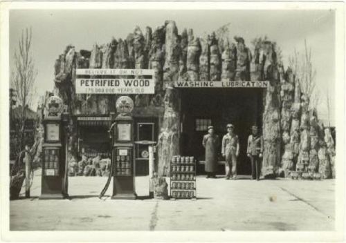 Historic gas station with a rock-like facade, featuring vintage pumps and two men standing outside.