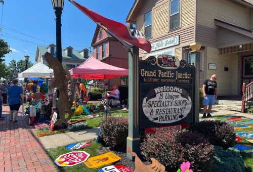 A bustling outdoor market at Grand Pacific Junction, featuring colorful signs, tents, and shoppers enjoying the historic district.