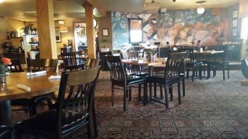Cozy restaurant interior with wooden tables, black chairs, and a colorful mural on the wall.
