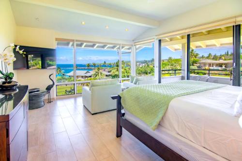 Bright bedroom with a view of the ocean, featuring a bed, seating area, and large windows letting in natural light.