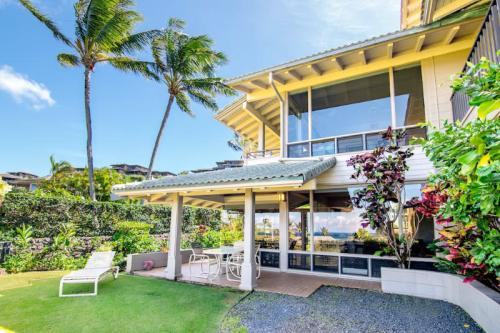 A tropical home with palm trees, a patio, and a view of the ocean, surrounded by lush greenery and blue skies.