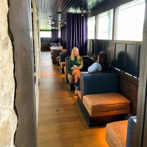 Two women sit in a cozy, well-lit restaurant booth, engaged in conversation along a stylish corridor.