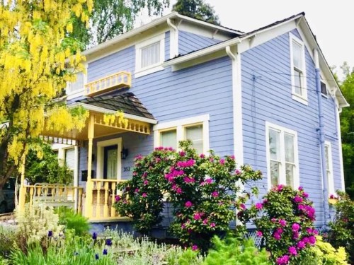 A charming blue house with yellow accents, surrounded by vibrant flowers and greenery.