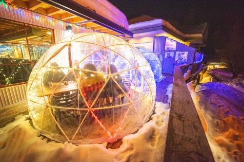 Cozy igloos with string lights on a snowy deck, creating a warm dining atmosphere at night.