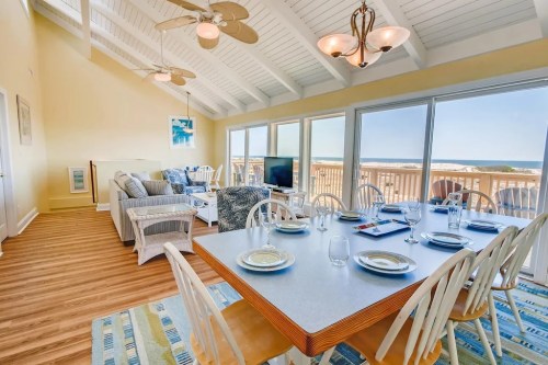 Bright, airy dining area with a table set for meals, overlooking a scenic view through large windows. Cozy living space nearby.