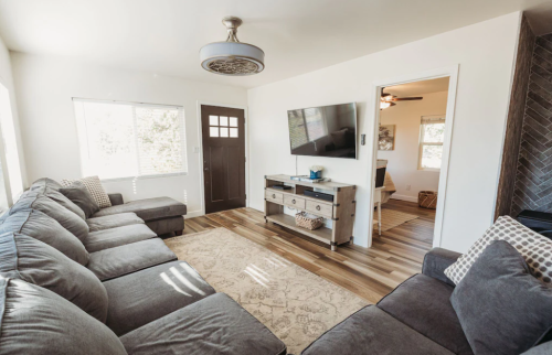 Cozy living room with a large sectional sofa, TV, and wooden console, featuring natural light from windows.