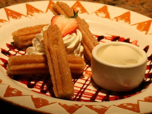 A plate of churros with whipped cream, a strawberry, and a scoop of vanilla ice cream drizzled with chocolate sauce.