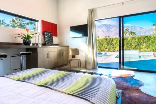 Modern bedroom with a striped blanket, a view of mountains, and a sliding glass door leading to a pool area.
