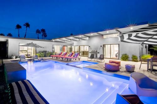 Modern outdoor space featuring a pool, lounge chairs, and a patio, illuminated at night with palm trees in the background.
