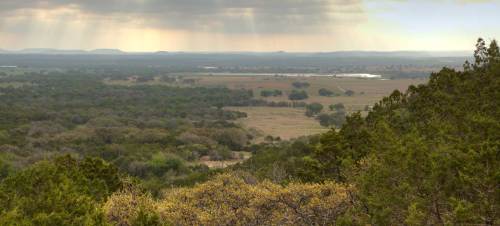 A panoramic view of a lush green landscape under a cloudy sky, with distant hills and a river visible.