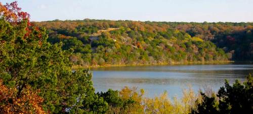 A serene lake surrounded by trees with autumn foliage, reflecting the colorful landscape under a clear sky.
