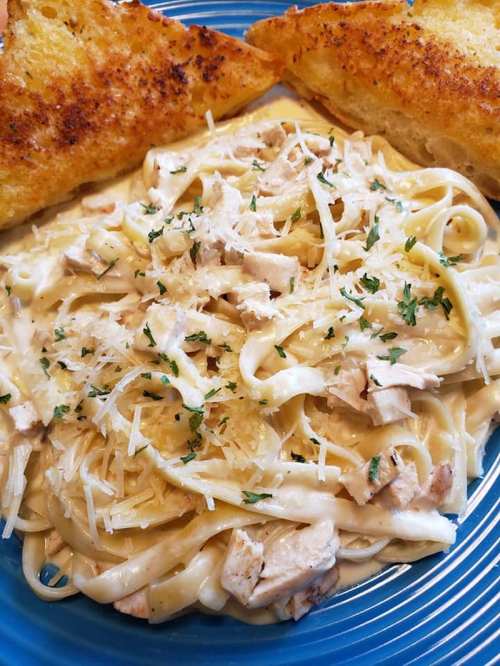 Creamy fettuccine alfredo with chicken, topped with parsley and parmesan, served with two slices of toasted garlic bread.