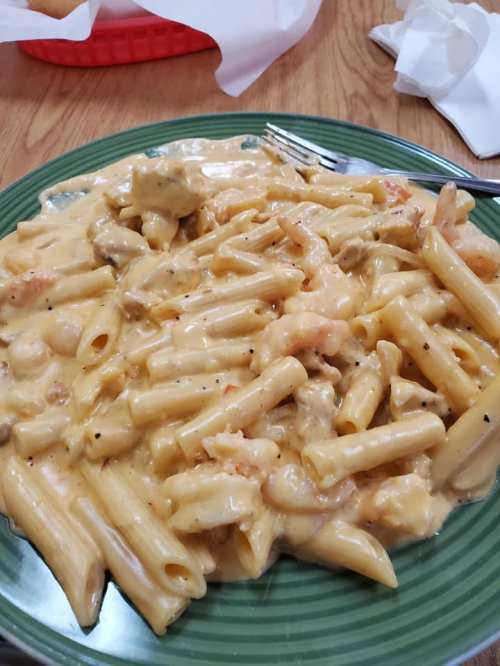 A plate of creamy pasta with shrimp and chicken, served on a green dish with a fork beside it.