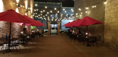 Outdoor dining area with red umbrellas, string lights, and tables, creating a cozy evening atmosphere.
