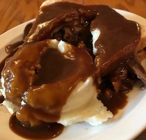 A plate of mashed potatoes topped with gravy, served with slices of bread and beef covered in brown sauce.