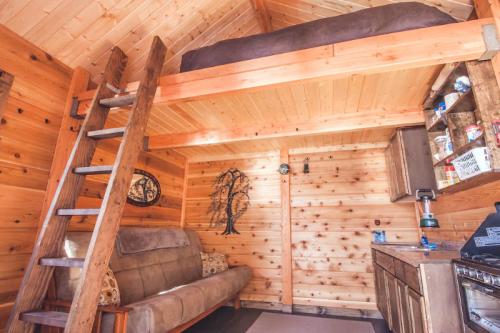 Cozy wooden interior of a cabin with a lofted bed, sofa, and kitchenette, featuring warm wood tones and rustic decor.