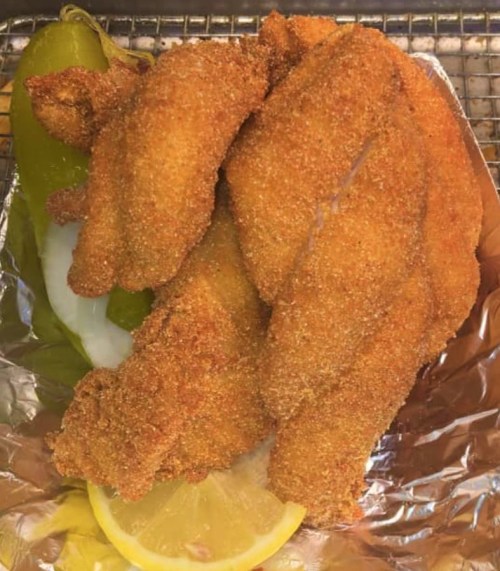 Crispy fried fish fillets on a bed of lettuce, garnished with a lemon slice and a green pepper.