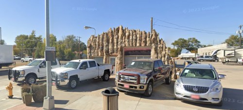 A parking lot with several trucks and cars, featuring a unique rock-like structure in the background.