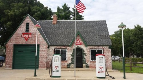 Historic Conoco gas station with vintage pumps, red brick exterior, and an American flag in front.