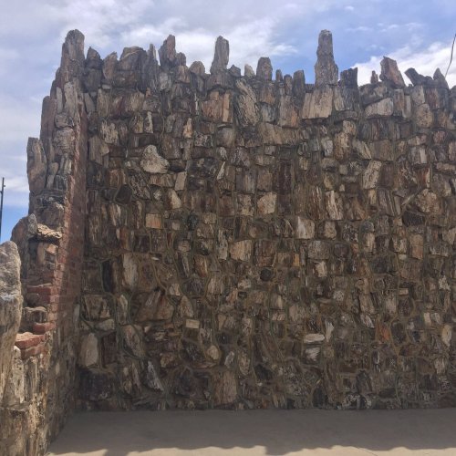 A textured stone wall made of irregularly shaped rocks, with a clear blue sky in the background.