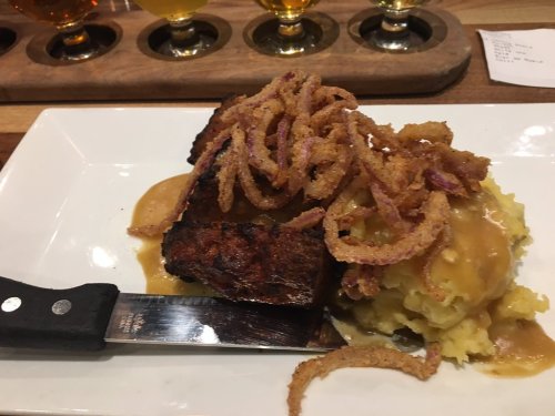 A plate of meatloaf topped with crispy onions, served with mashed potatoes and gravy, alongside a flight of beers.