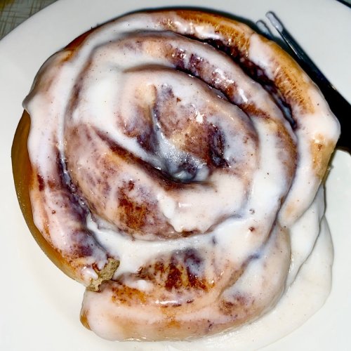 A close-up of a cinnamon roll topped with creamy icing on a white plate.