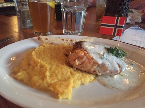 A plate of salmon with creamy sauce, served with yellow mashed potatoes and a small Norwegian flag.
