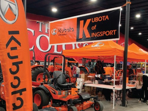 A display for Kubota of Kingsport featuring orange tractors and equipment under a tent at an indoor event.